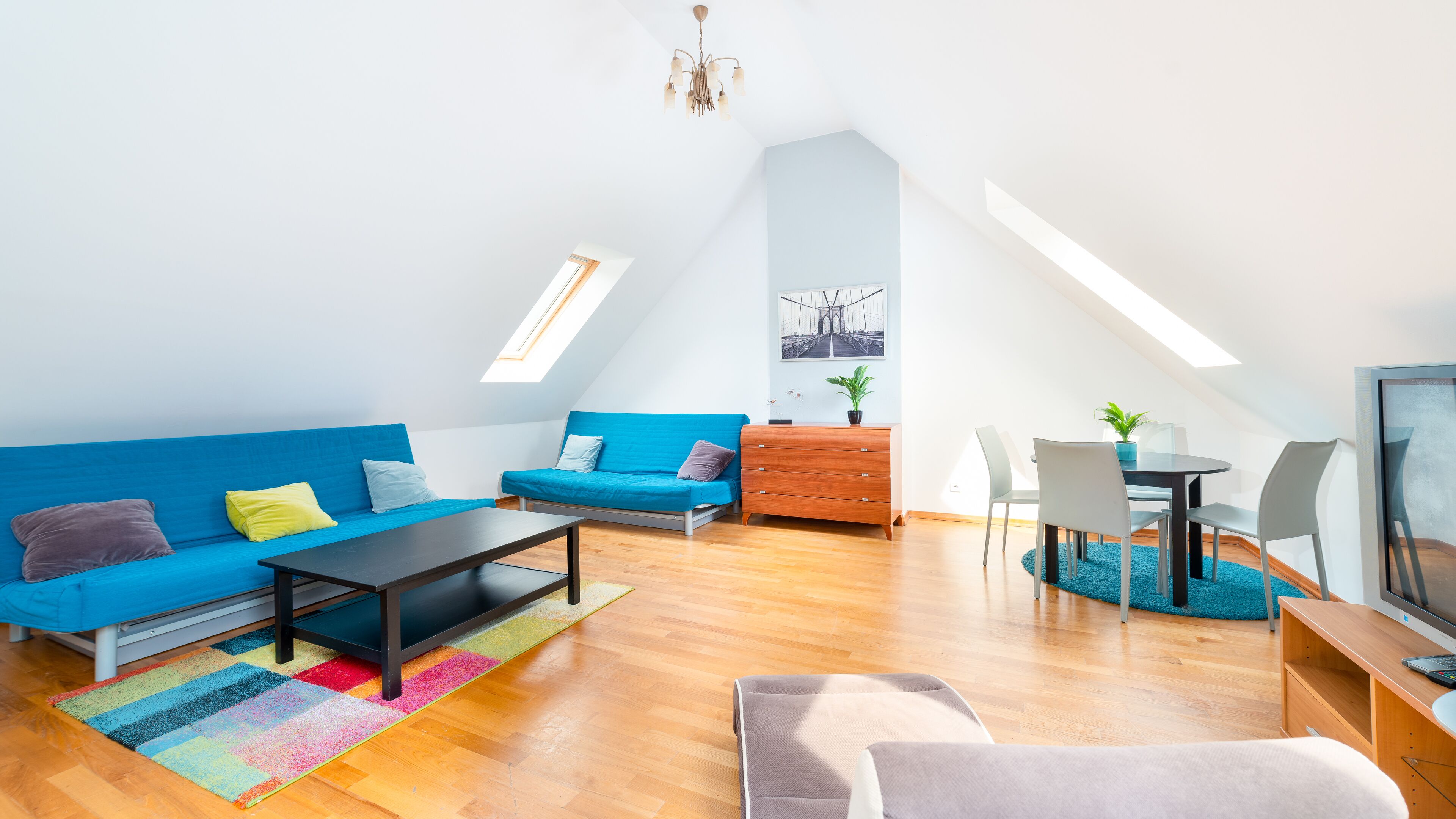 Un moderno loft con soffitto alto, un lucernario, un divano blu, un tavolo da pranzo in legno e una televisione.