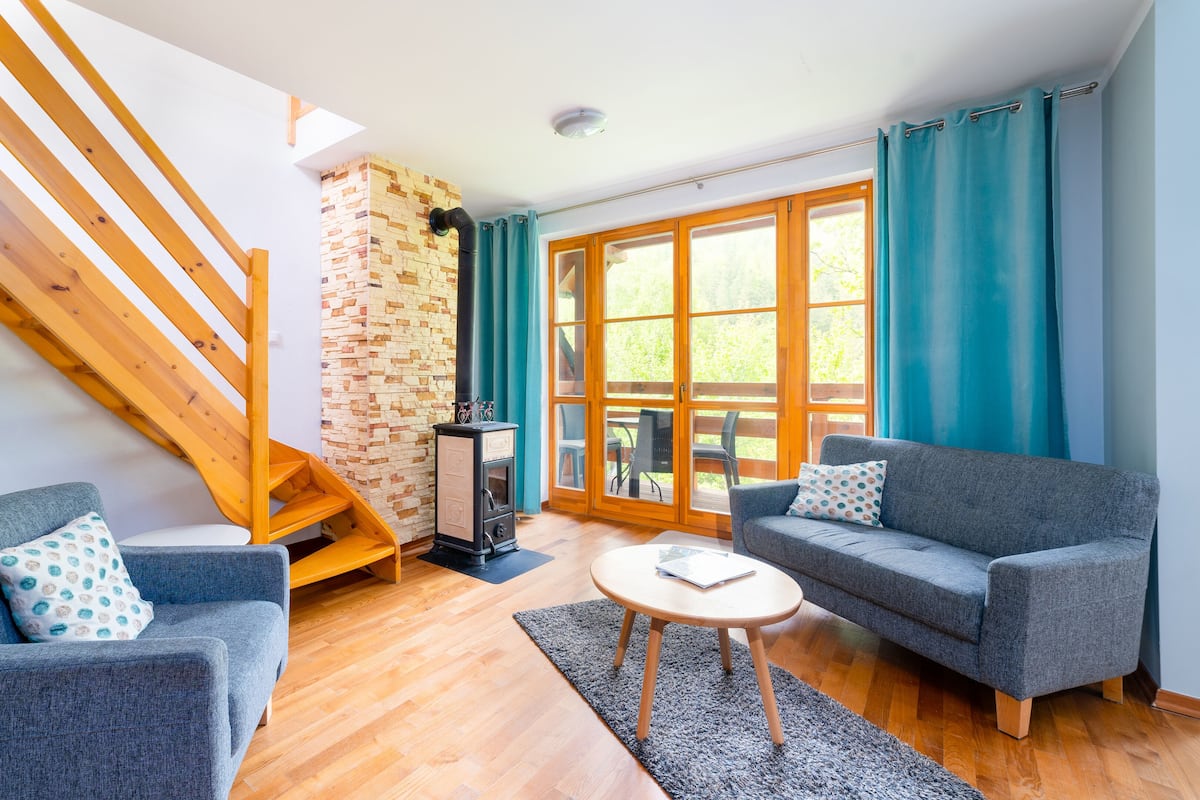 A modern living room with a staircase, two grey sofas, a small round table, and a stone wall.