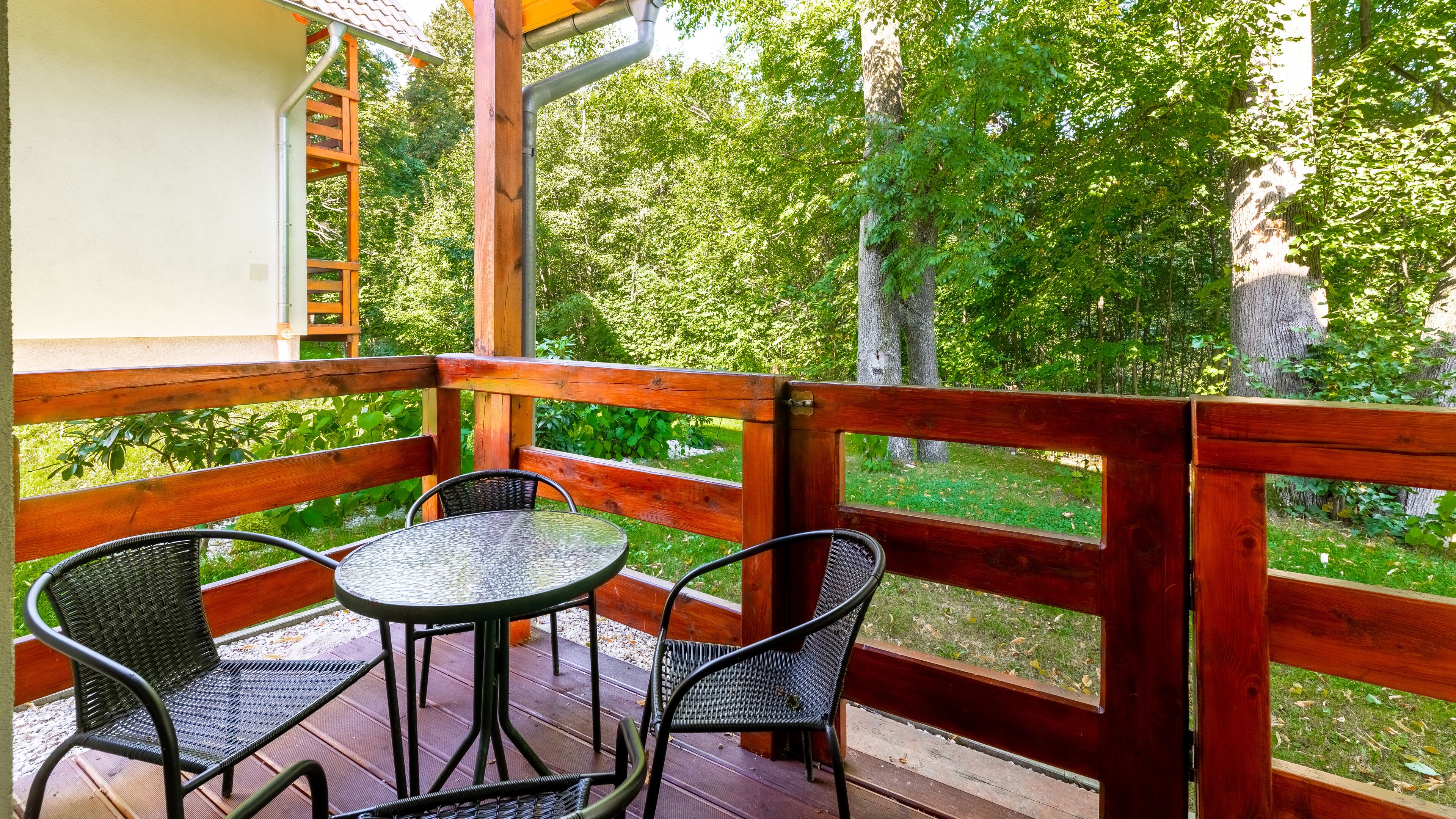 Un terrazzo in legno con tavolo e due sedie, affacciato su un paesaggio verde e rigoglioso.