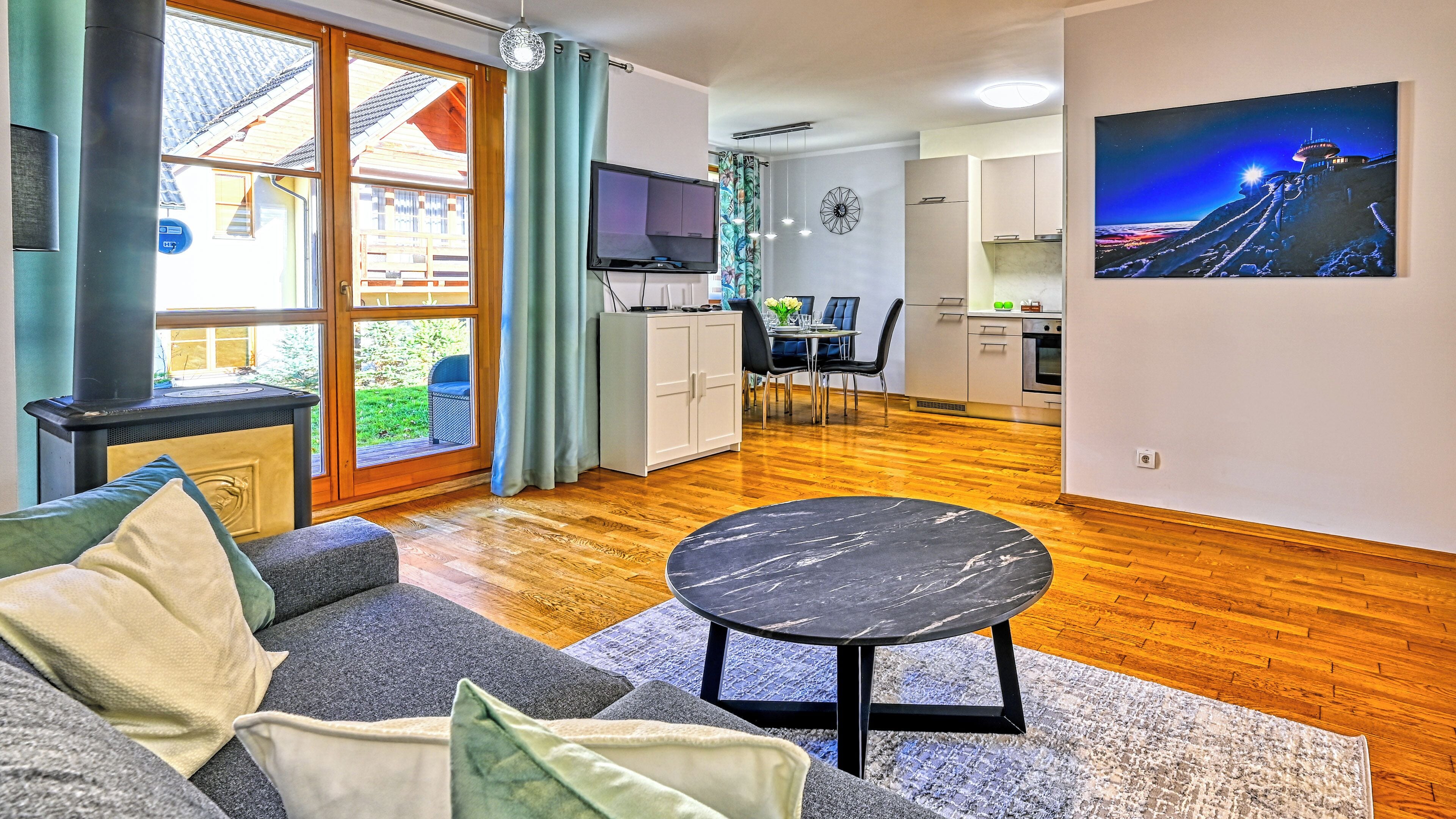 Uma sala de estar moderna com um sofá, uma mesa de centro redonda e uma área de jantar com mesa e cadeiras.
