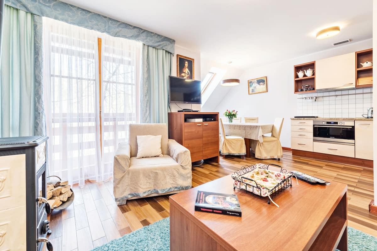 A modern living room with a sofa, a coffee table, a TV, and a kitchen area with cabinets and a stove.