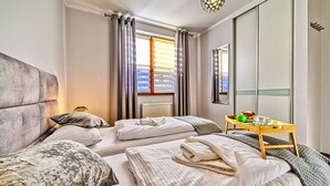A hotel room with two beds, a wooden side table with a green apple and a glass, and a window with blinds. - Apartamenty Sun & Snow Karpacz Myśliwska (Karpacz)