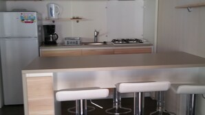 Una cocina compacta con refrigerador, cafetera y estufa a gas. Hay tres taburetes blancos en la barra.
