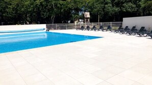 Una piscina con agua azul cristalina, rodeada por una terraza de baldosas y varias sillas de descanso.