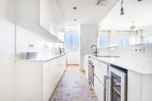 A modern kitchen with white cabinetry, a patterned tile floor, and a view of the sky through large windows.