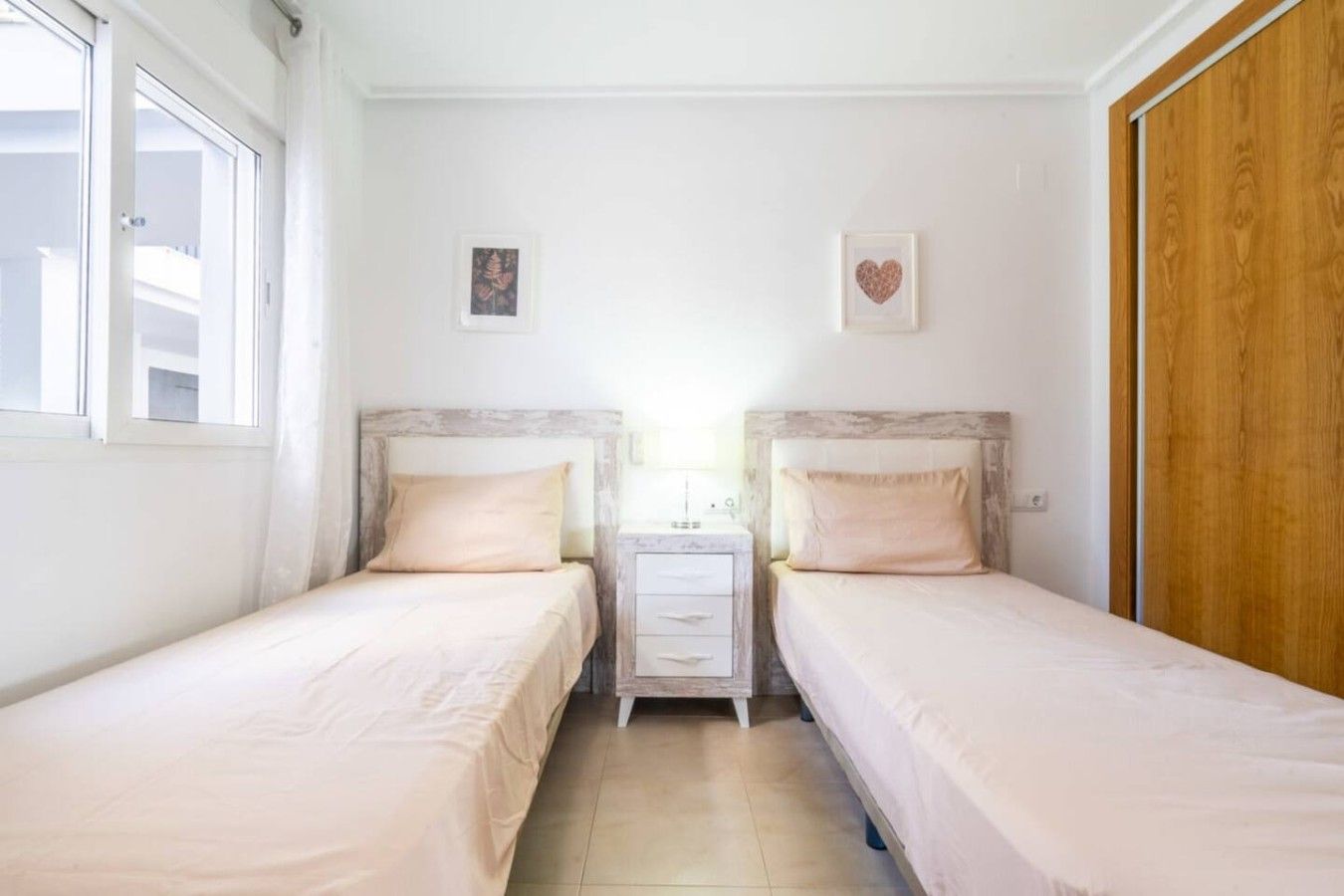 Une chambre avec deux lits simples, une table de chevet, une armoire et une fenêtre.