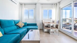 Una sala de estar moderna con un sofá color turquesa, una mesa de centro de madera y un comedor con una mesa y sillas blancas.