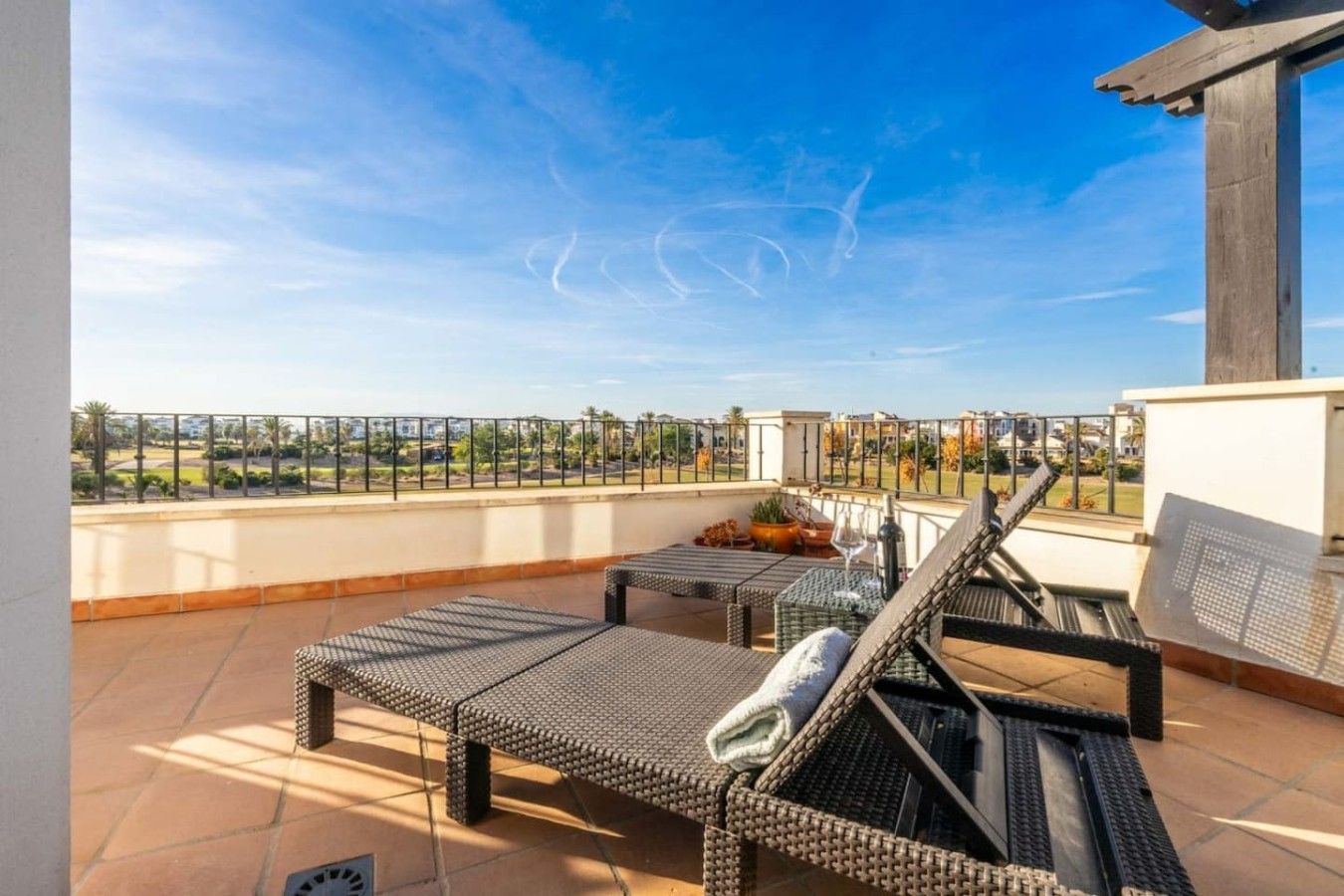 A rooftop terrace with two sun loungers, a small table with a glass, and a view of a landscaped area.