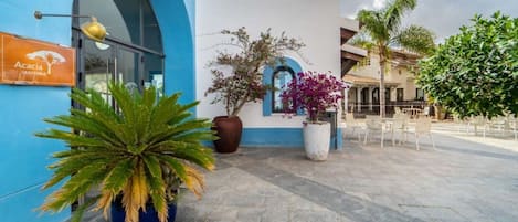 A building with a blue facade, a sign reading 'Acacia Trattoria,' and outdoor seating area with chairs and tables.