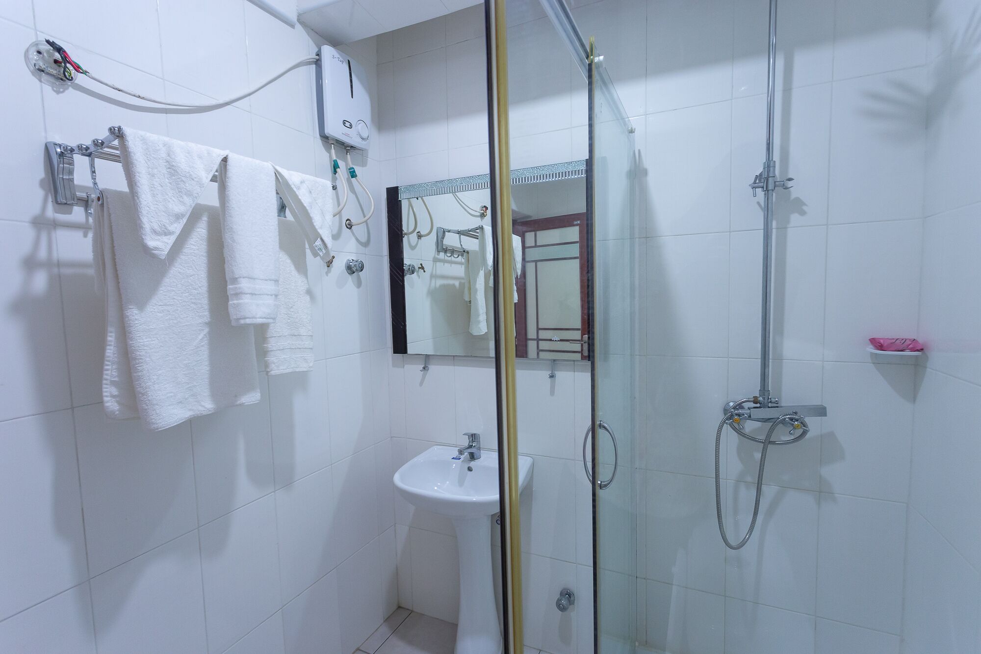 Un baño con cabina de ducha de vidrio, un lavabo y un perchero con varias toallas.