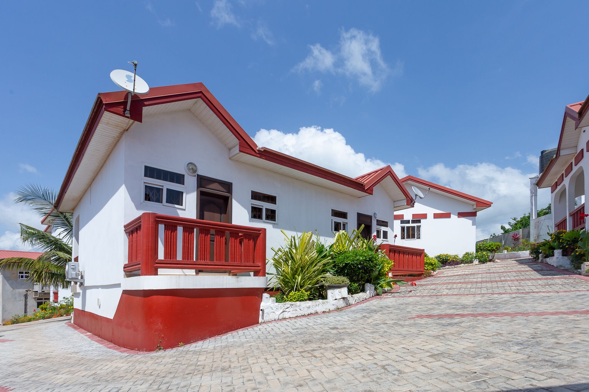 A two-story house with a red and white exterior, satellite dishes, and a paved driveway.