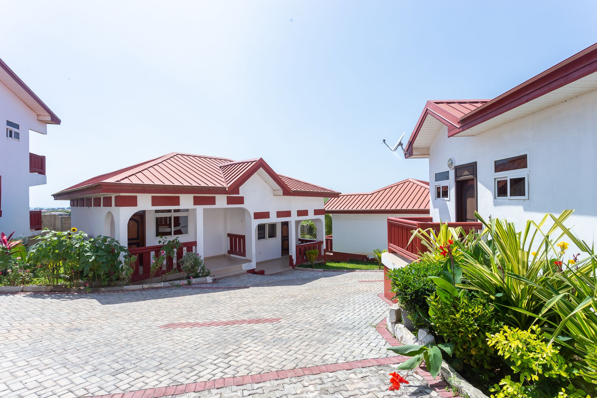 Un barrio residencial con casas de techos rojos y paredes blancas, un patio empedrado y abundante vegetación circundante.