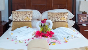 A neatly made bed with white and brown patterned pillows, a bouquet of flowers, and folded towels. - Royal Elmount Hotel (Elmina)