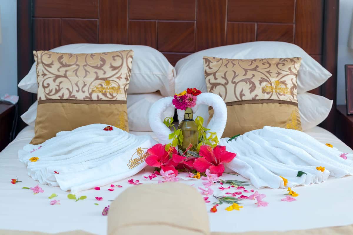 A neatly made bed with white and brown patterned pillows, a bouquet of flowers, and folded towels.
