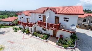 A two-story building with a red roof and white walls, featuring balconies and satellite dishes. - Royal Elmount Hotel (Elmina)