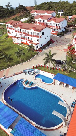 Un hotel con varias edificaciones, piscina y un área ajardinada con palmeras.