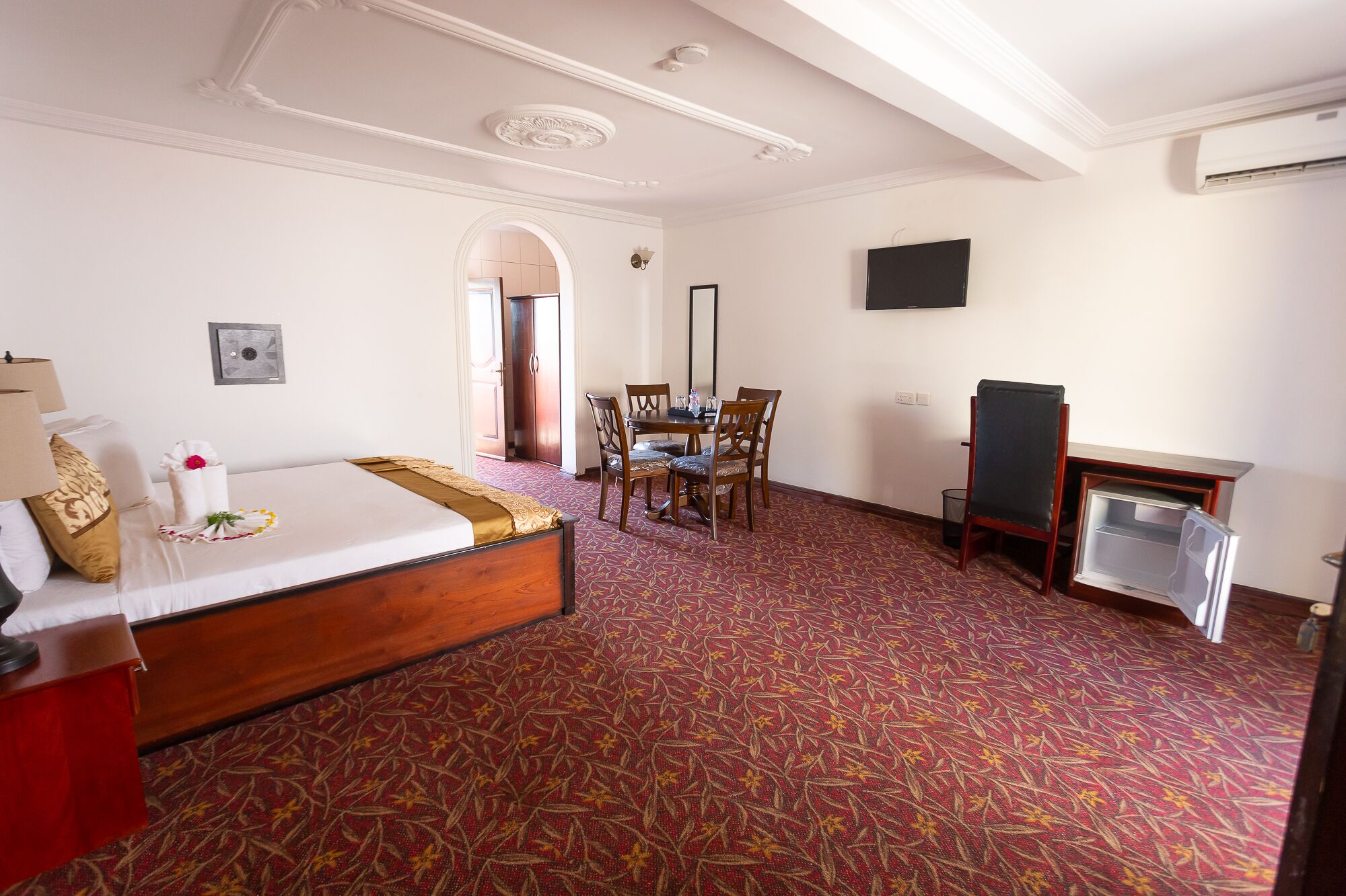 Habitación de hotel con cama, escritorio, silla, televisor y piso alfombrado.