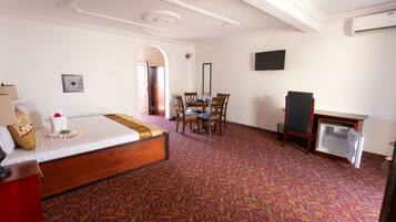 Habitación de hotel con cama, escritorio, silla, televisor y piso alfombrado.