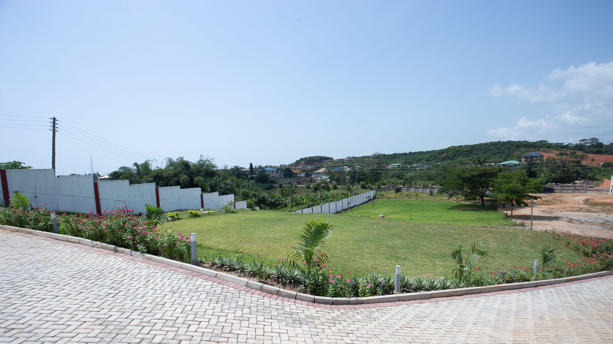 A paved area with a grassy field and a low wall.