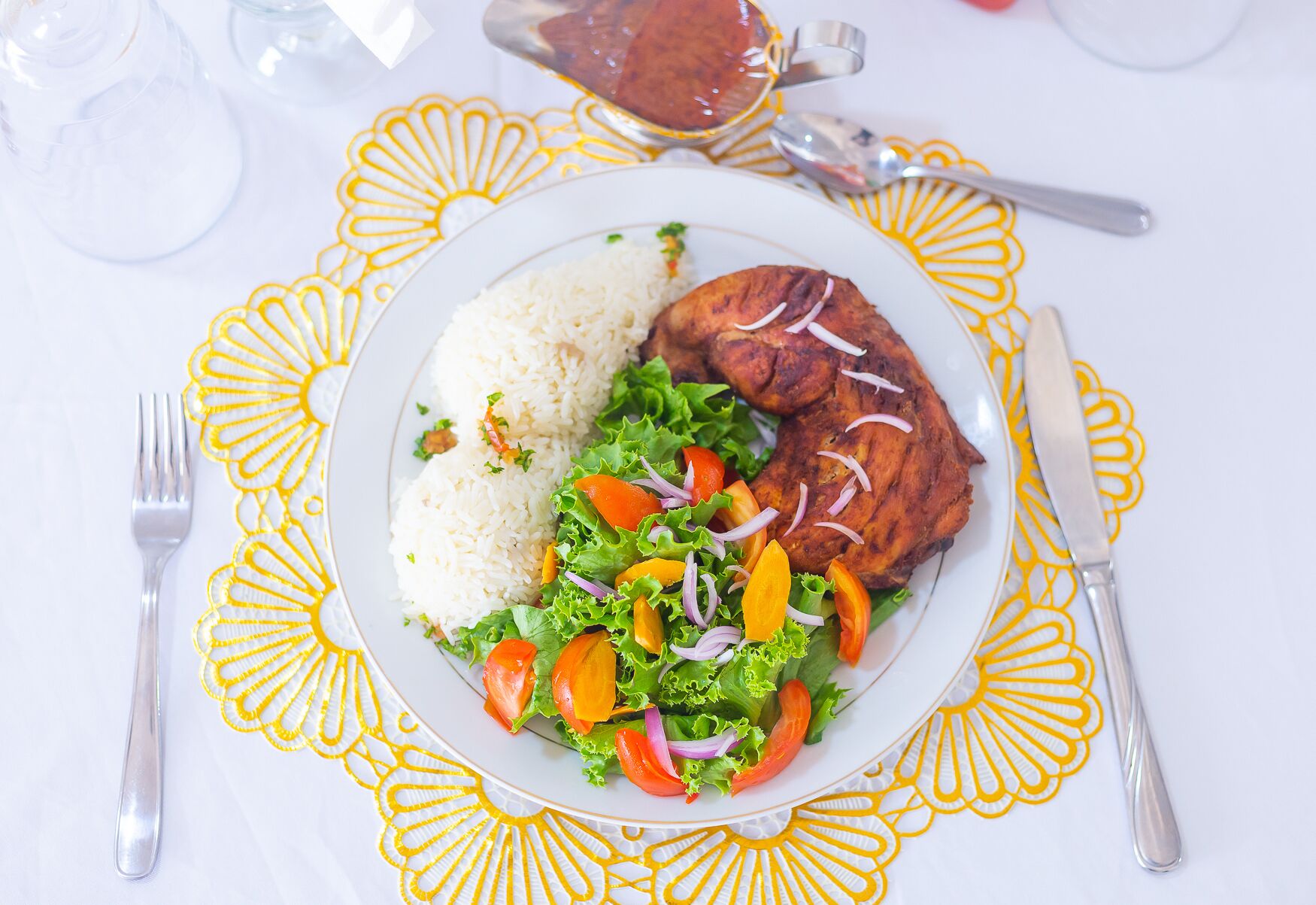 A plate of food with rice, grilled meat, and a salad on a table with a decorative tablecloth.
