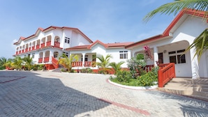 A two-story building with a red and white exterior, multiple balconies, and a paved courtyard. - Royal Elmount Hotel (Elmina)