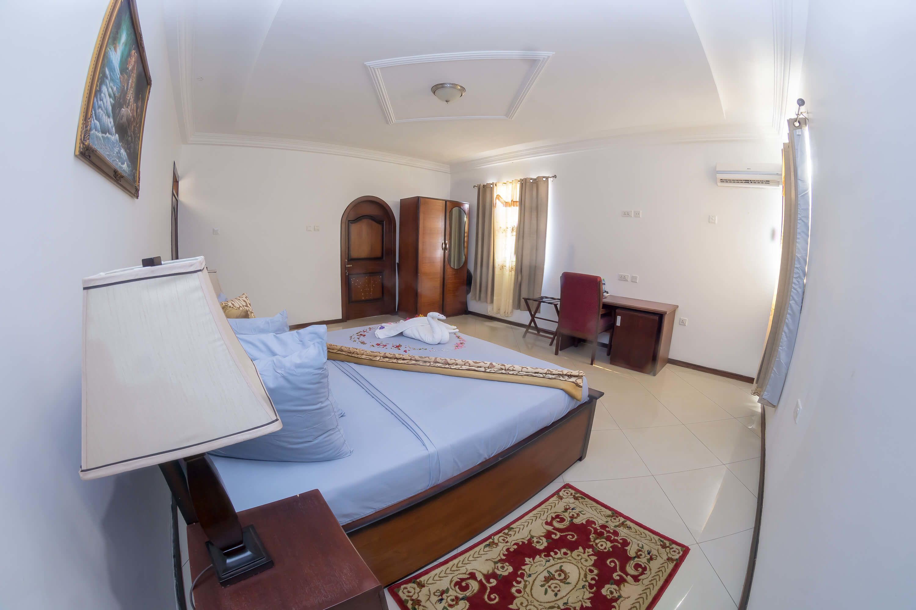 A hotel room with a bed, a desk, a chair, a wardrobe, and a mirror.