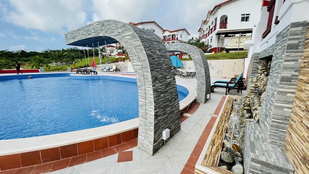 A swimming pool with stone arches, outdoor seating, and a view of nearby buildings. - Royal Elmount Hotel (Elmina)