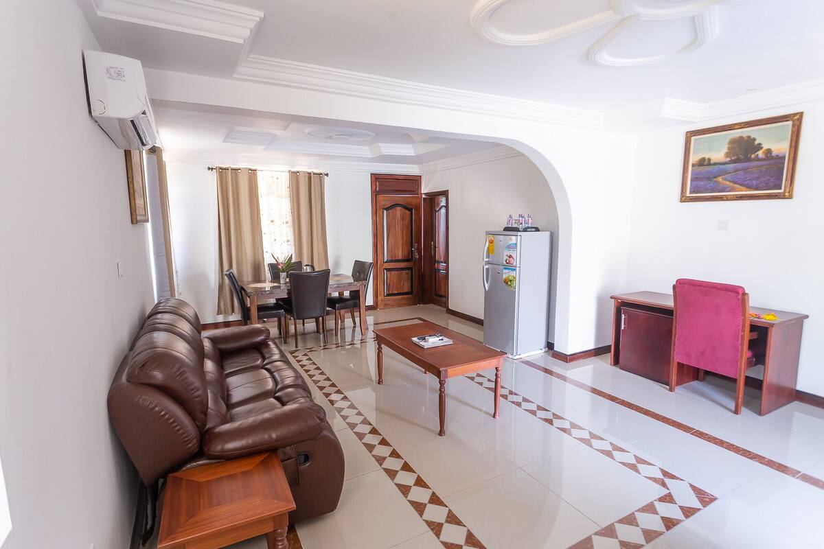 A living room with a brown leather sofa, a wooden coffee table, and a dining area with a table and chairs.