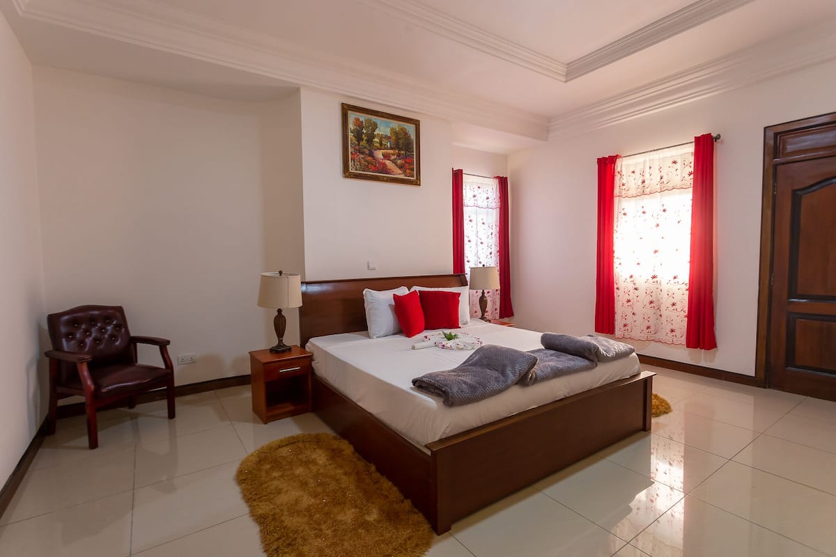 A neatly arranged bedroom with a large bed, a chair, a nightstand, and a painting on the wall.