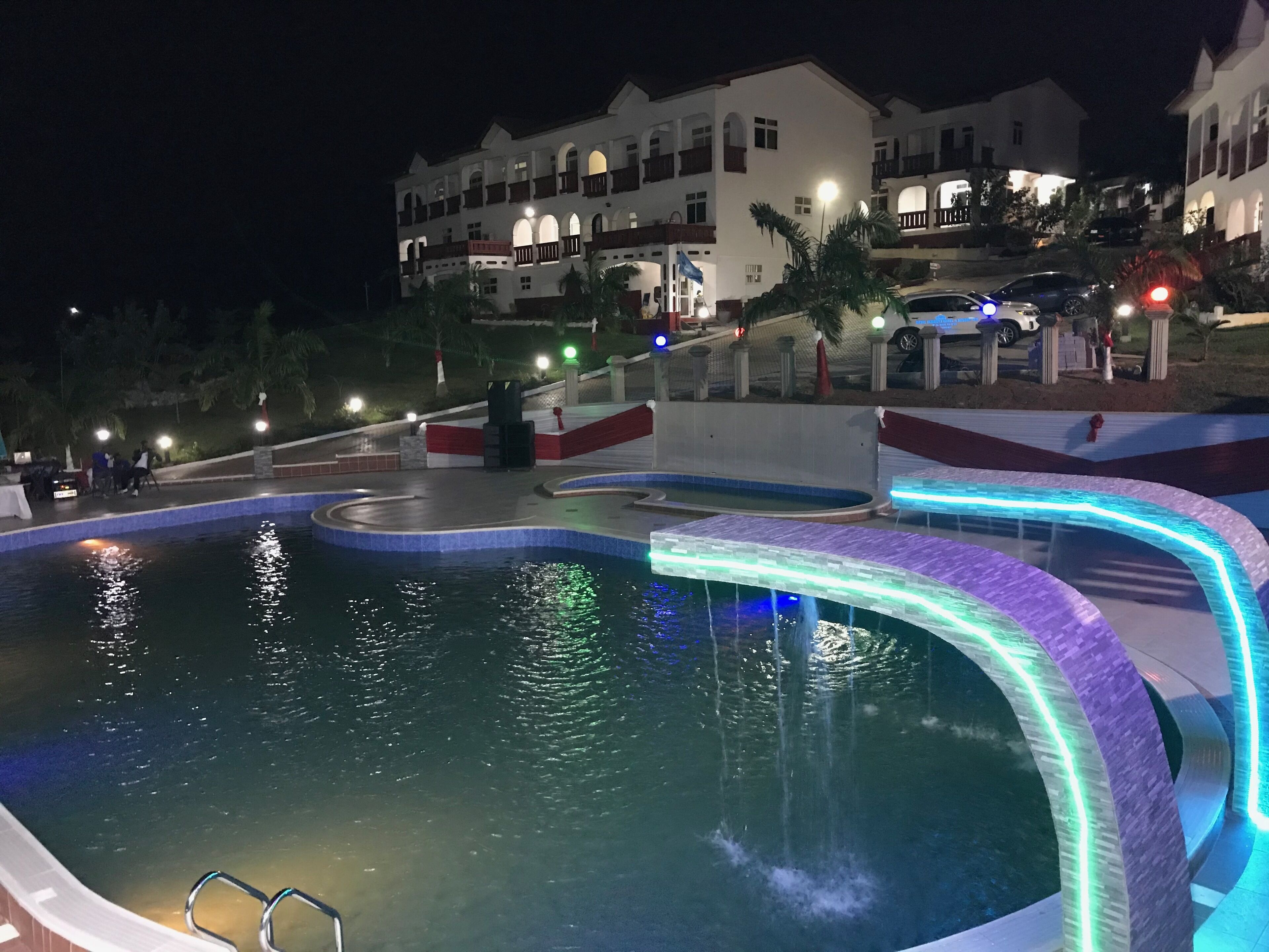 Una piscina con fuente acuática, rodeada por un edificio blanco con balcones y un diseño rojo y blanco.