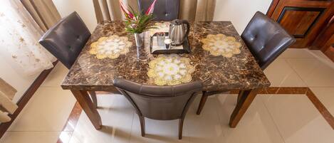 A dining table with four chairs, a coffee pot, and a decorative centerpiece.