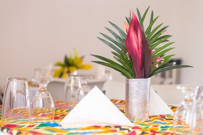 Una mesa con mantel colorido, jarrones de vidrio transparente y una planta decorativa en un florero texturizado.