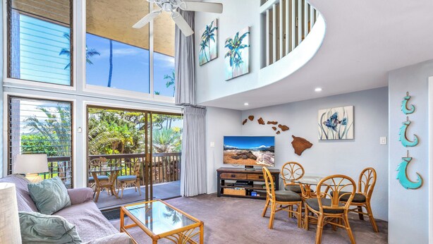 Un salón amplio con un gran ventanal, un ventilador de techo, un televisor y un comedor con mobiliario de mimbre.