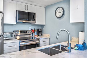 A modern kitchen with white cabinets, stainless steel appliances, a microwave, oven, and a sink with a faucet.
