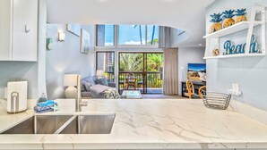 Una sala de estar moderna con un ventanal grande, una cocina con encimera de mármol y un balcón con mobiliario exterior.