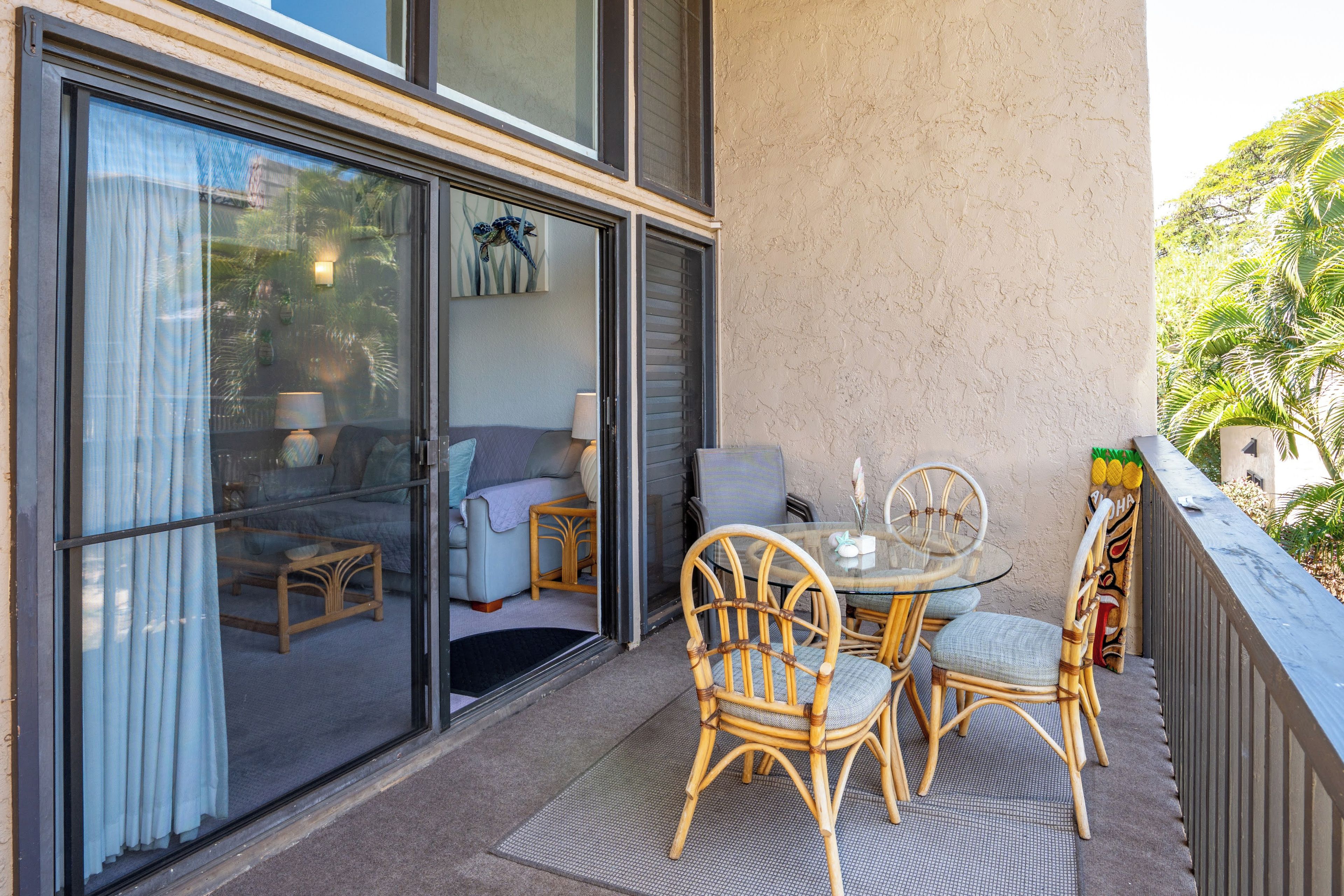A balcony with wicker chairs, a glass table, and a view of the interior through a sliding glass door.