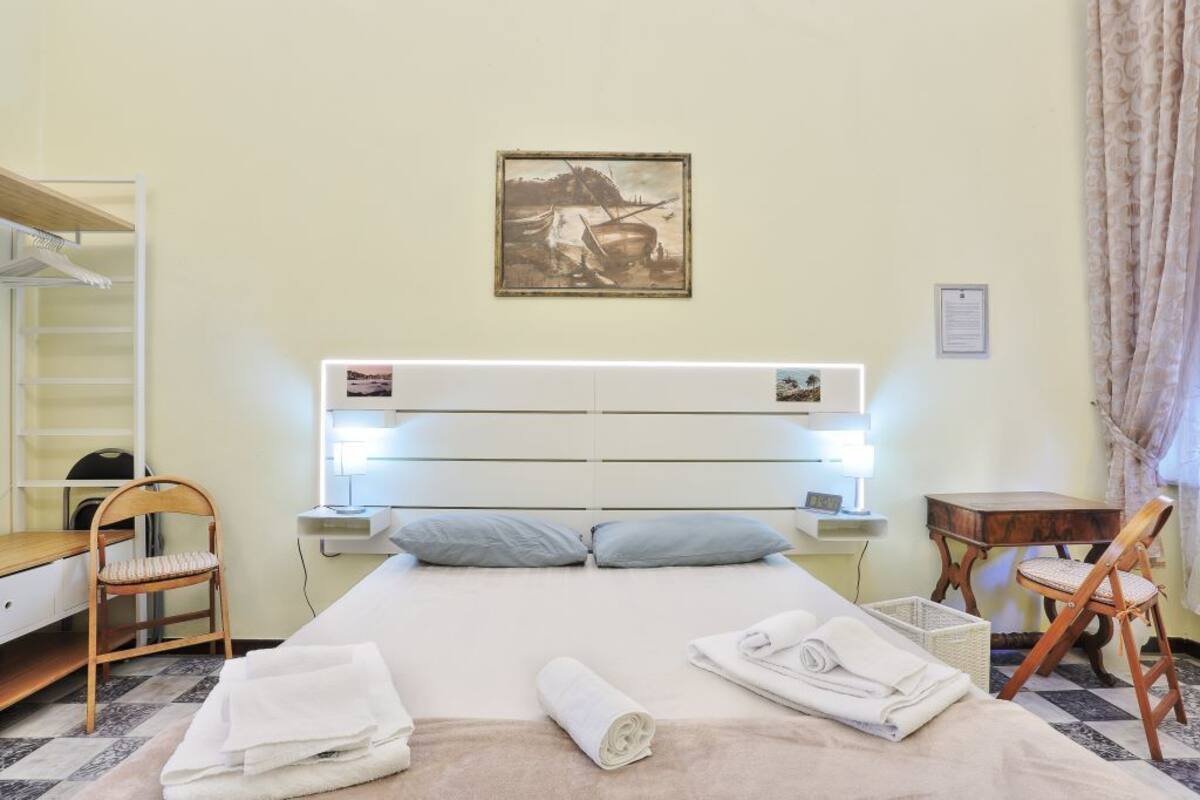 Une chambre d’hôtel bien rangée, avec un lit, un bureau, une chaise et une petite table.
