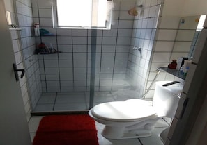 Ein Badezimmer mit Toilette, rotem Teppich und Duschbereich.