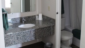 A bathroom with a granite countertop sink, a mirror, a toilet, and a shower curtain. - Arbour Ridge Inn & Suites (Kindersley)