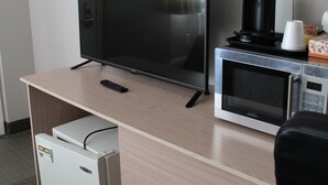 A hotel room with a TV, a microwave, a coffee maker, a lamp, and a mini-fridge. - Arbour Ridge Inn & Suites (Kindersley)