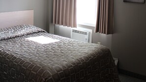 A bedroom with a bed, a window with curtains, a radiator, and a wall-mounted picture. - Arbour Ridge Inn & Suites (Kindersley)