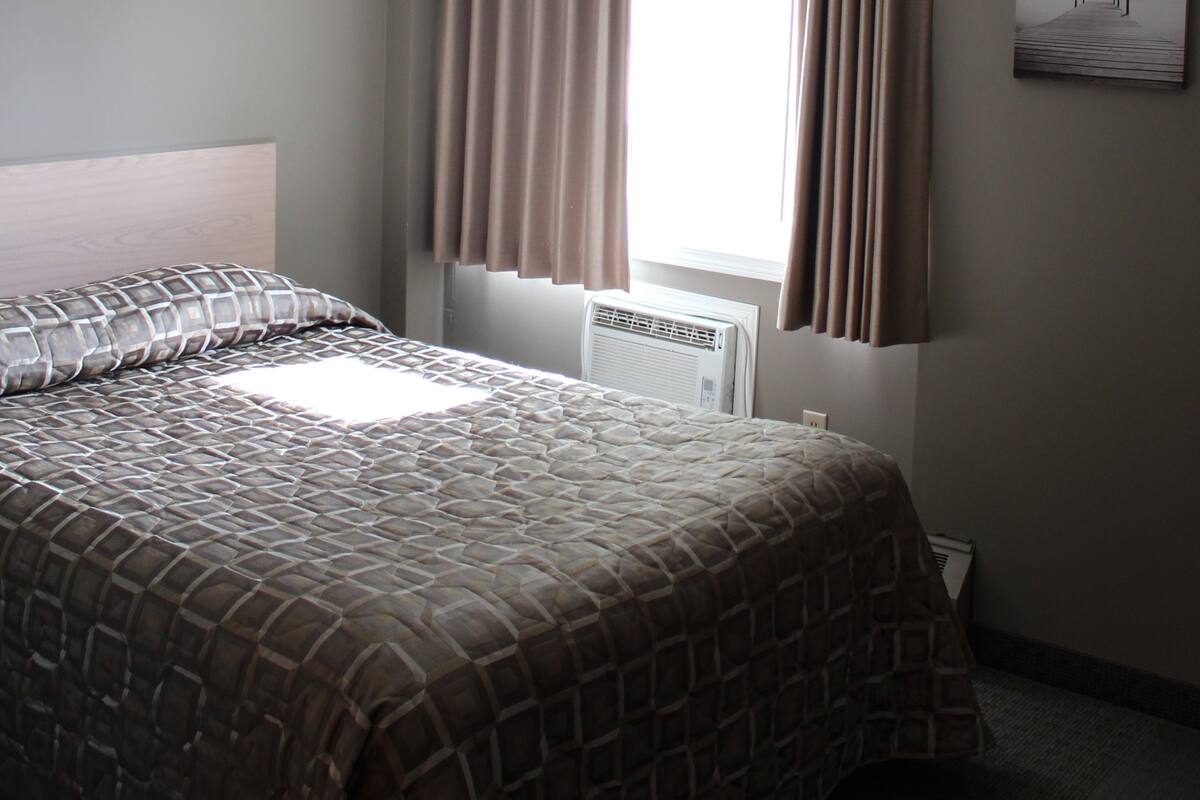 A bedroom with a bed, a window with curtains, a radiator, and a wall-mounted picture.