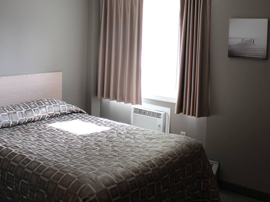 A bedroom with a bed, a window with curtains, a radiator, and a wall-mounted picture.