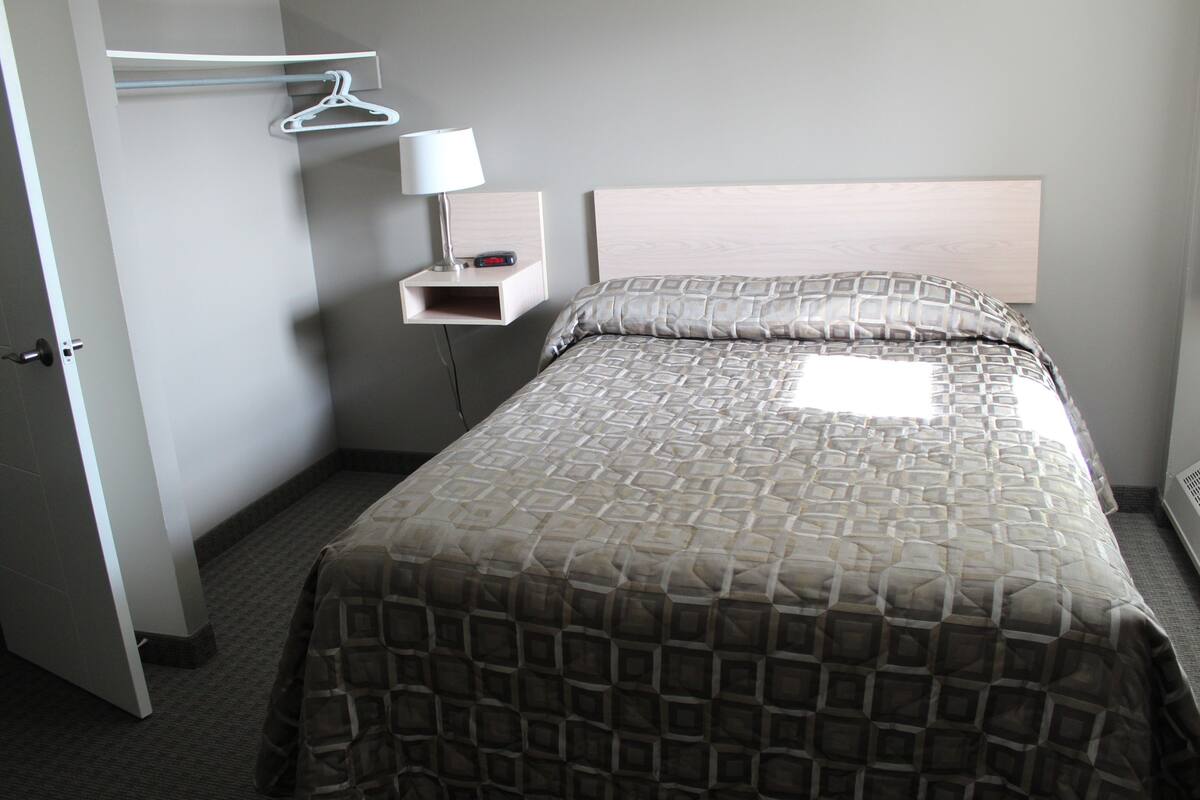 A hotel room with a bed, a bedside table with a lamp, a hanging coat rack, and a wardrobe.