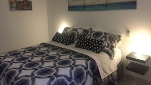 Ett sovrum med en säng, mönstrat sänglinne, en tavla som föreställer en stadsbild och ett nattduksbord med en lampa.