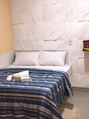 A hotel room with a patterned headboard, a bed with a blue and white striped bedspread, and a small table with a bag of snacks. - Pousada Executive Express - Próximo ao Aeroporto (Goiania)