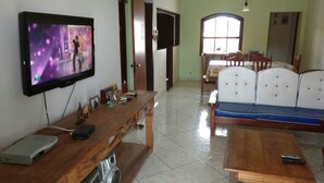 Ein Wohnzimmer mit Fernseher, Holzmöbeln, einer Couch und einem Essbereich mit Stühlen und Tisch.