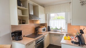 A compact kitchen with a microwave, stove, and coffee maker. - Vacation home Lueg, holiday apartment rental North Sea - Holiday home Lueg (Varel)