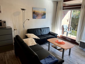 A modern living room with a black leather sofa, a small wooden table, and a floor lamp. A painting of a beach scene hangs on the wall.