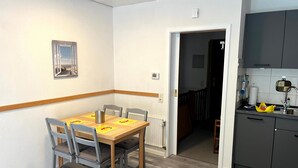 Un comedor con mesa y sillas de madera, un radiador, y una cocina con armarios y un lavamanos.